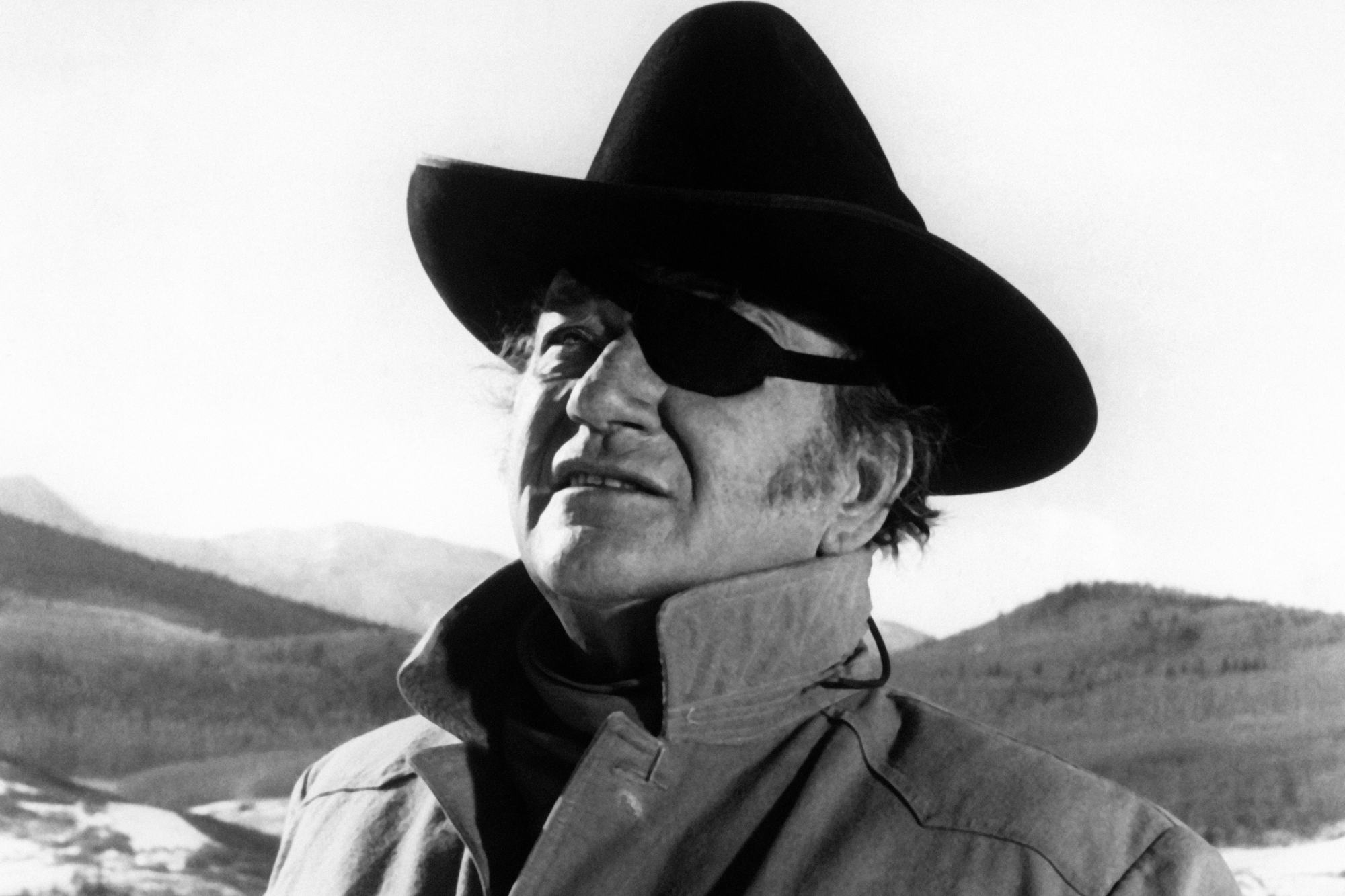'True Grit' John Wayne as Rooster Cogburn in a black-and-white picture, wearing a cowboy hat and eyepatch.