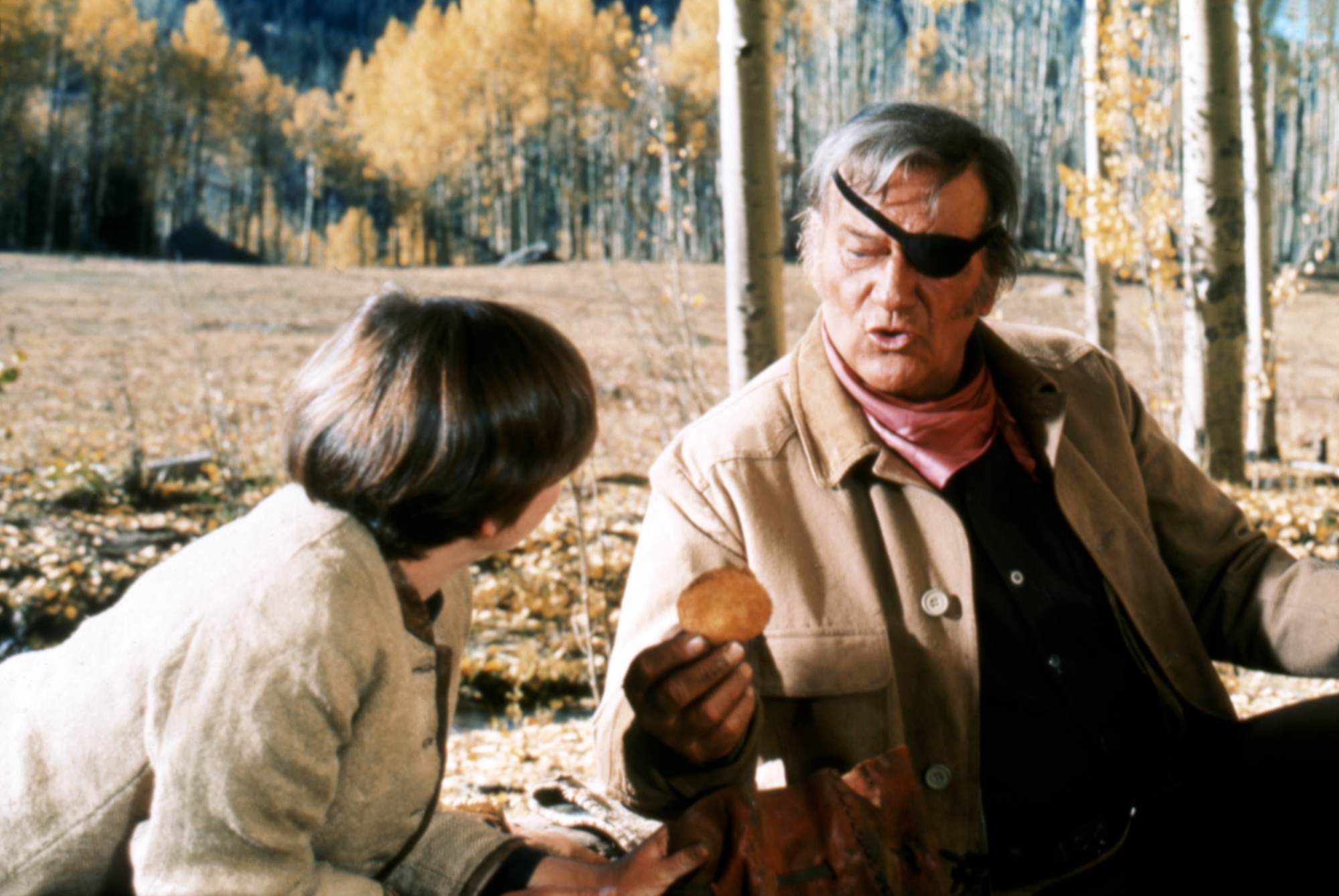 'True Grit' Kim Darby as Mattie Ross and John Wayne as Rooster Cogburn sitting in the woods.