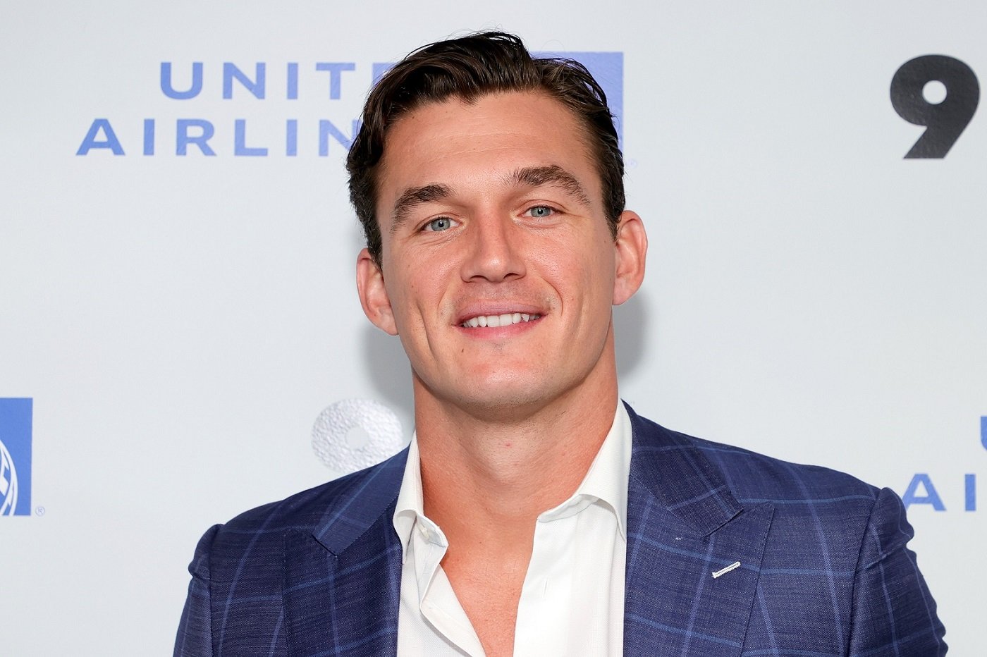 A close-up of Tyler Cameron smiling while wearing a white shirt and blue blazer