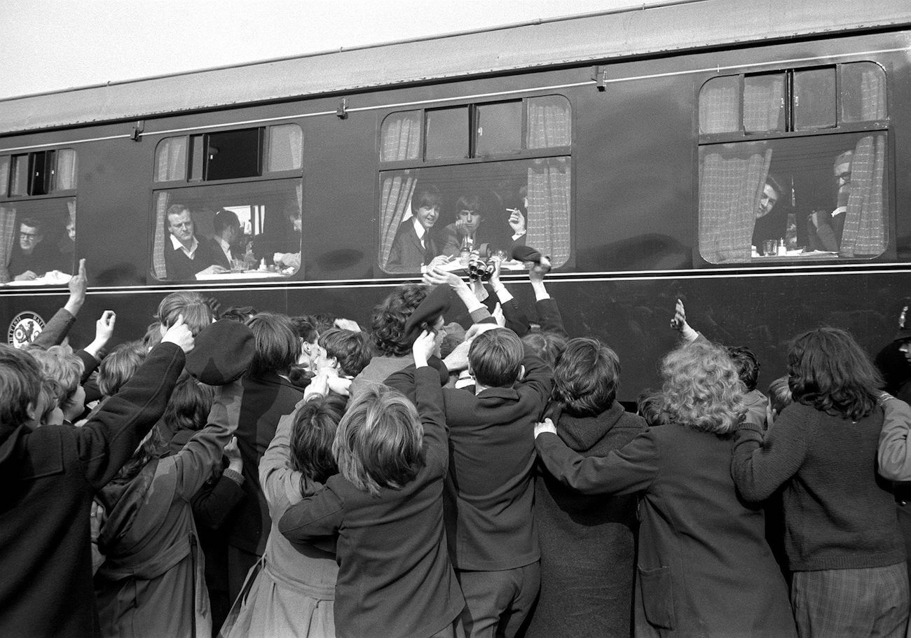 The Beatles on a train with fans waving goodbye.