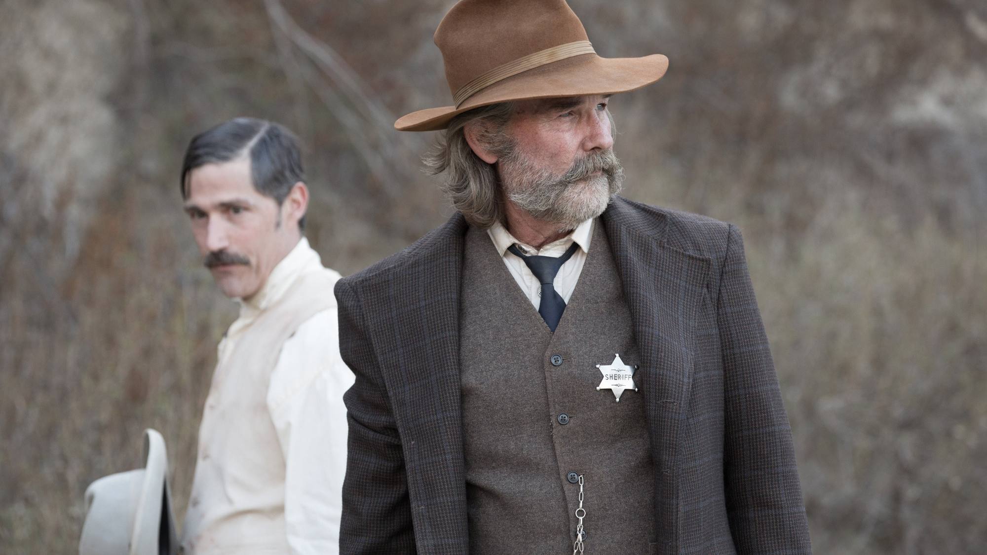 Western horror 'Bone Tomahawk' Matthew Fox as Brooder and Kurt Russell as Sheriff Hunt looking in opposite directions wearing Western clothes. Fox standing behind Russell.
