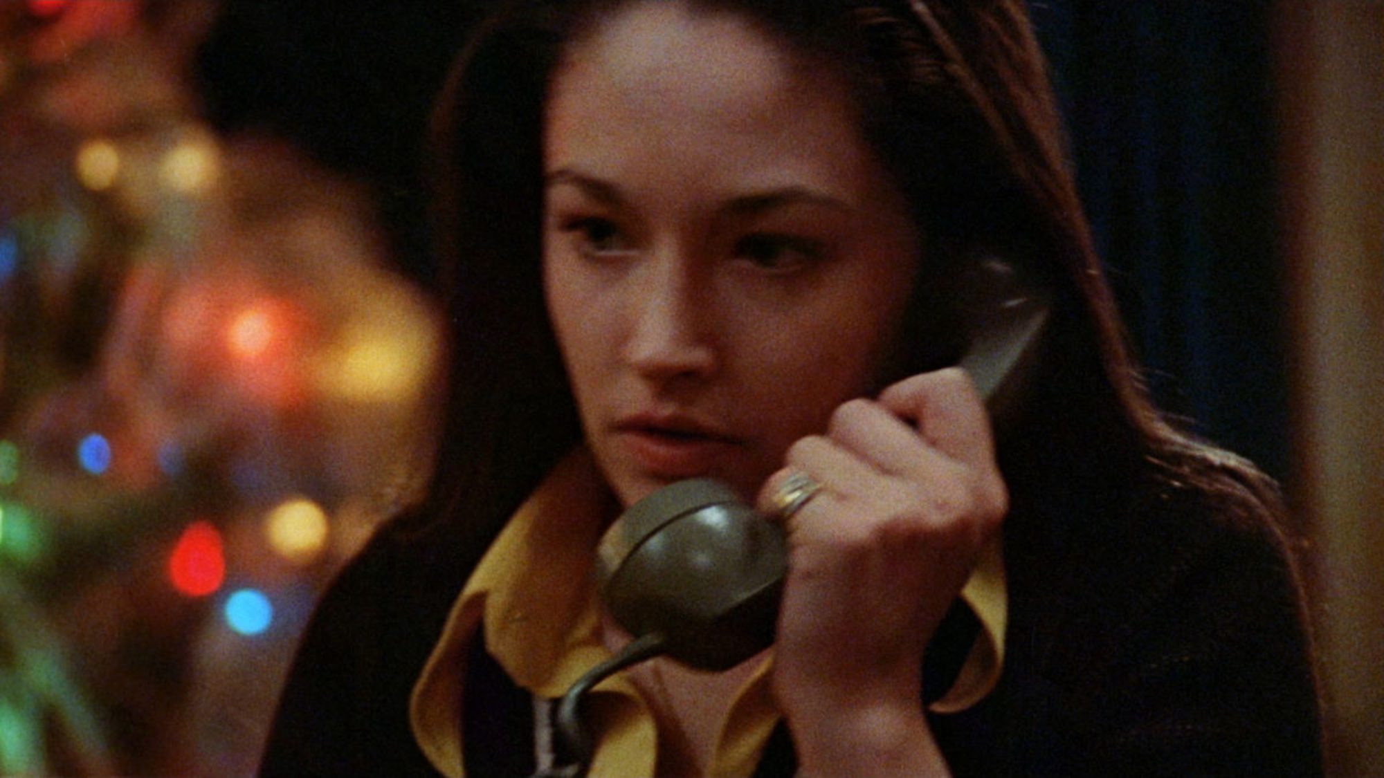 Whodunit movies 'Black Christmas' Olivia Hussey as Jess holding a phone with Christmas lights on in the background.