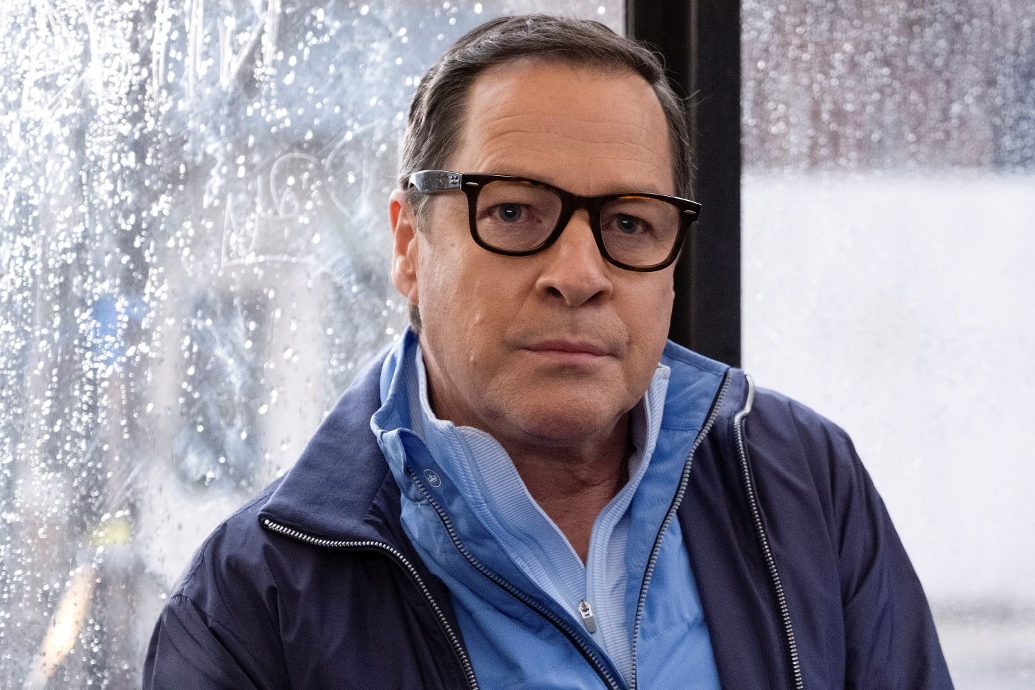 French Stewart, in character as Lenny Broussard in 'Will Trent' Season 1 Episode 10, wears a dark blue coat over a light blue zip-up jacket and black-framed glasses.