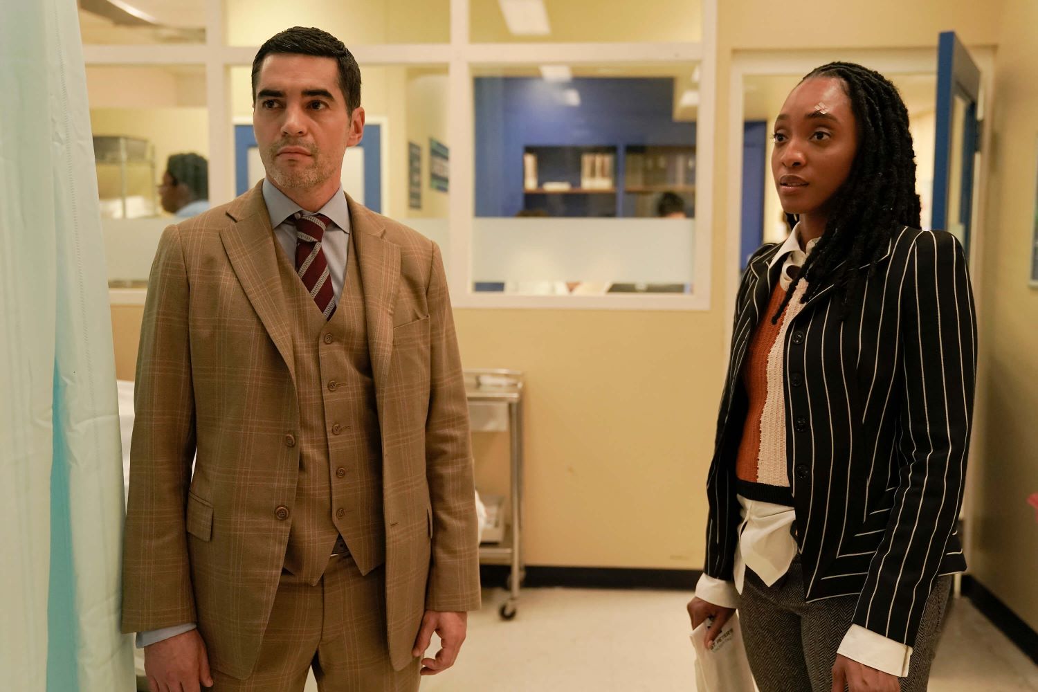 Ramón Rodríguez as Will Trent and Iantha Richardson as Faith Mitchell in 'Will Trent' on ABC, which hasn't been renewed for season 2 yet. Will wears a tan three-piece suit over a light gray button-up shirt and maroon and white striped tie. Faith wears a black suit with thin white stripes over a brown and white sweater vest over a white button-up shirt and gray pants.