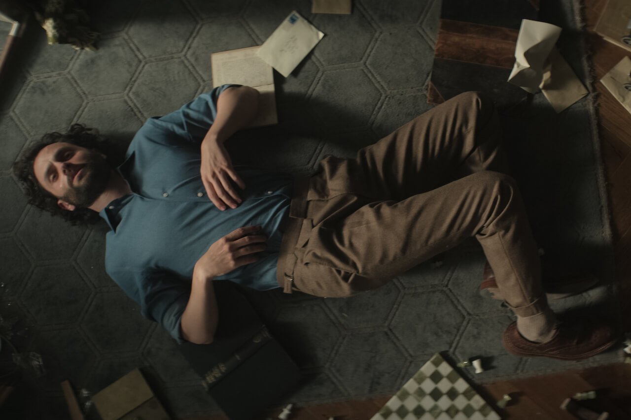 Penn Badgley as Joe Goldberg on 'You' Season 4 lies on the floor with paper next to him.