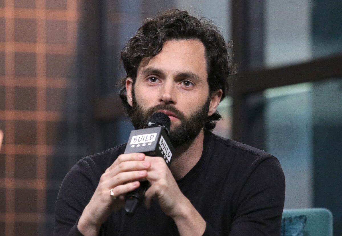 "You" star Penn Badgley speaking into a microphone during an interview.