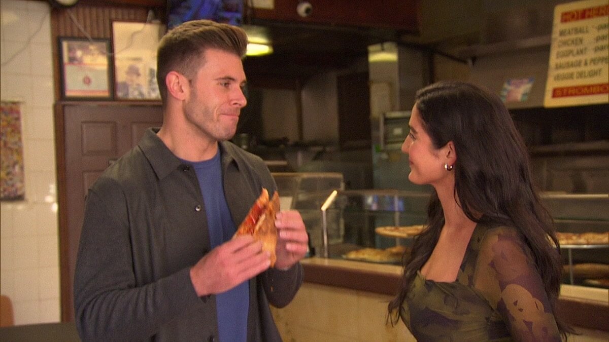 Zach Shallcross holding a pizza smiling at Ariel who is also smiling