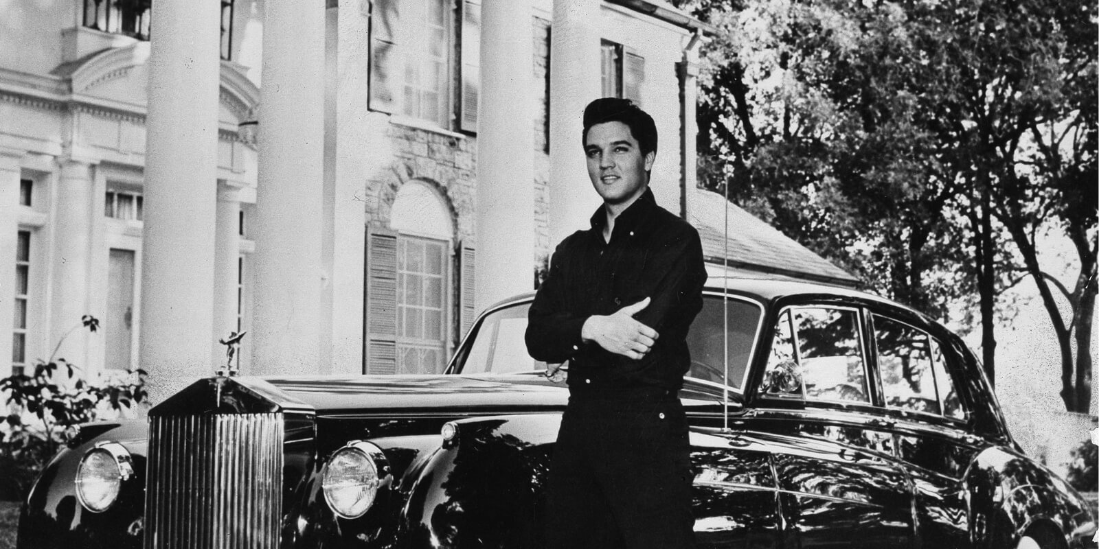 A black and white photo of Elvis Presley taken outside of his home Graceland in Memphis, TN.