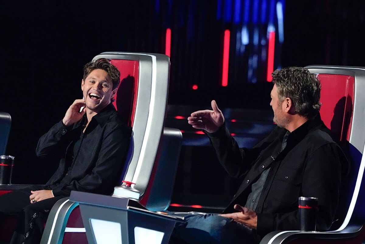 Niall Horan laughs at Blake Shelton as they sit in their chairs on The Voice Season 23.