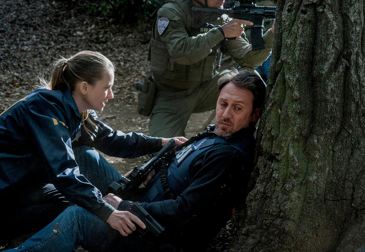 Criminal Minds: Evolution: A.J. Cook as JJ kneeling over Josh Stewart as William LaMontagne, who leans against a tree