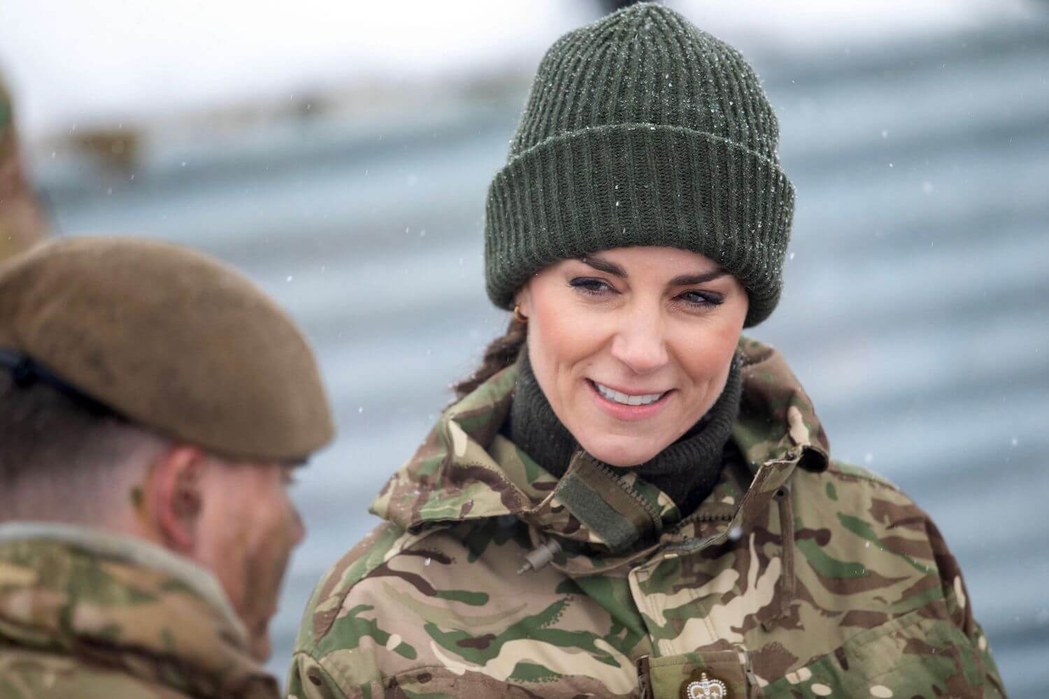 Kate Middleton smiles while wearing a camouflage top and a knit hat