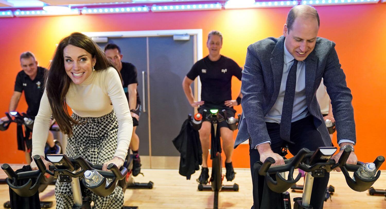 Kate Middleton and Prince William smiling while competing in a spin bike challenge