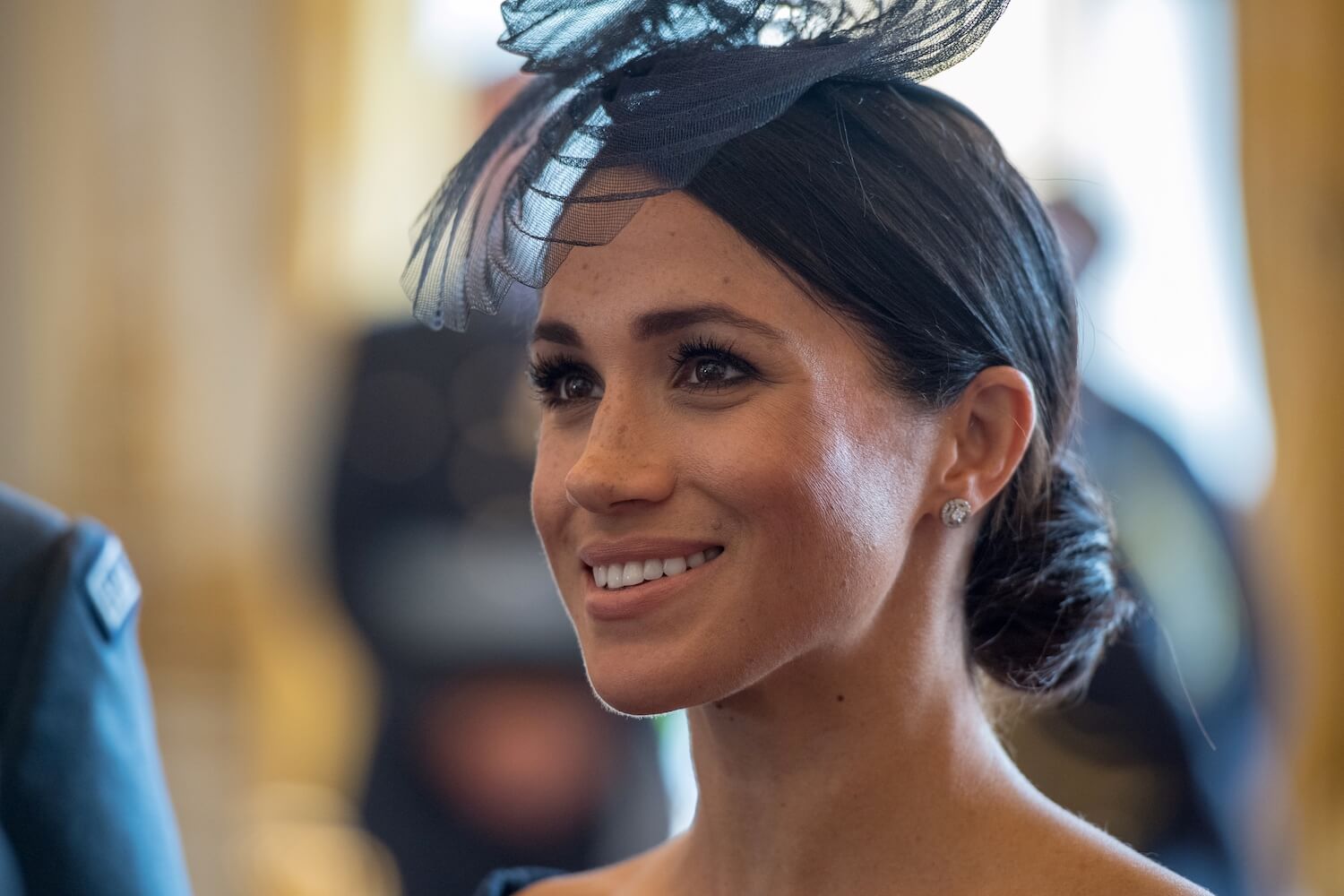 Meghan Markle smiles while wearing a black fascinator hat