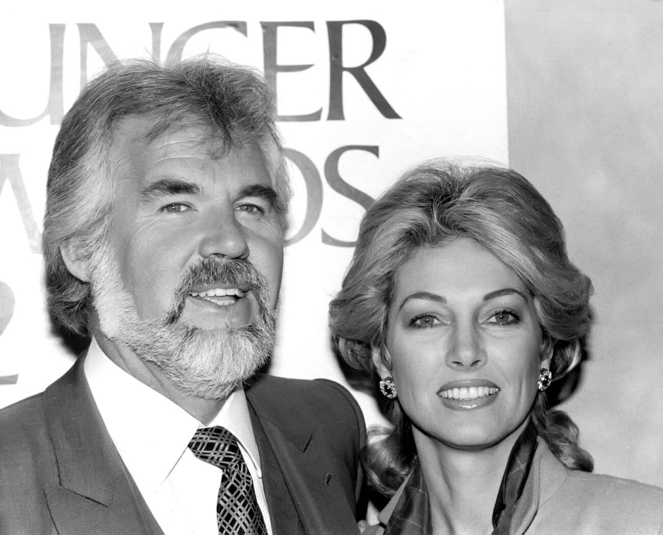 A black and white picture of Kenny Rogers and his wife Marianne Gordon posing in front of a sign.