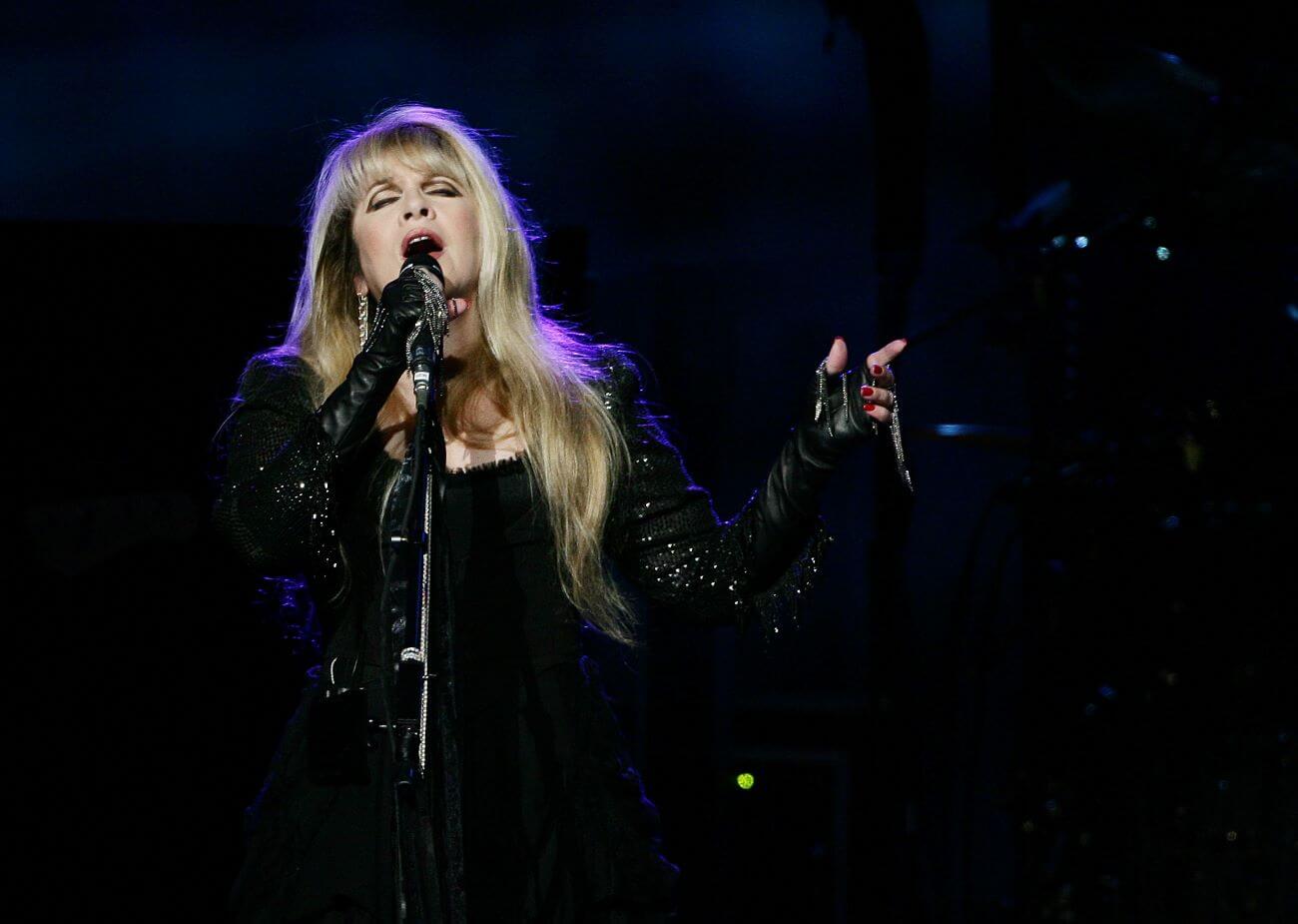 Stevie Nicks wears black and sings into a microphone.