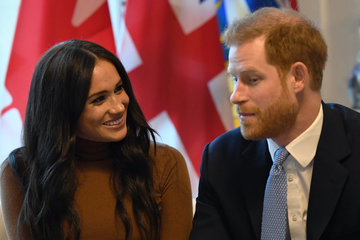 Meghan Markle wears a brown top as she looks at Prince Harry and smiles while he looks on