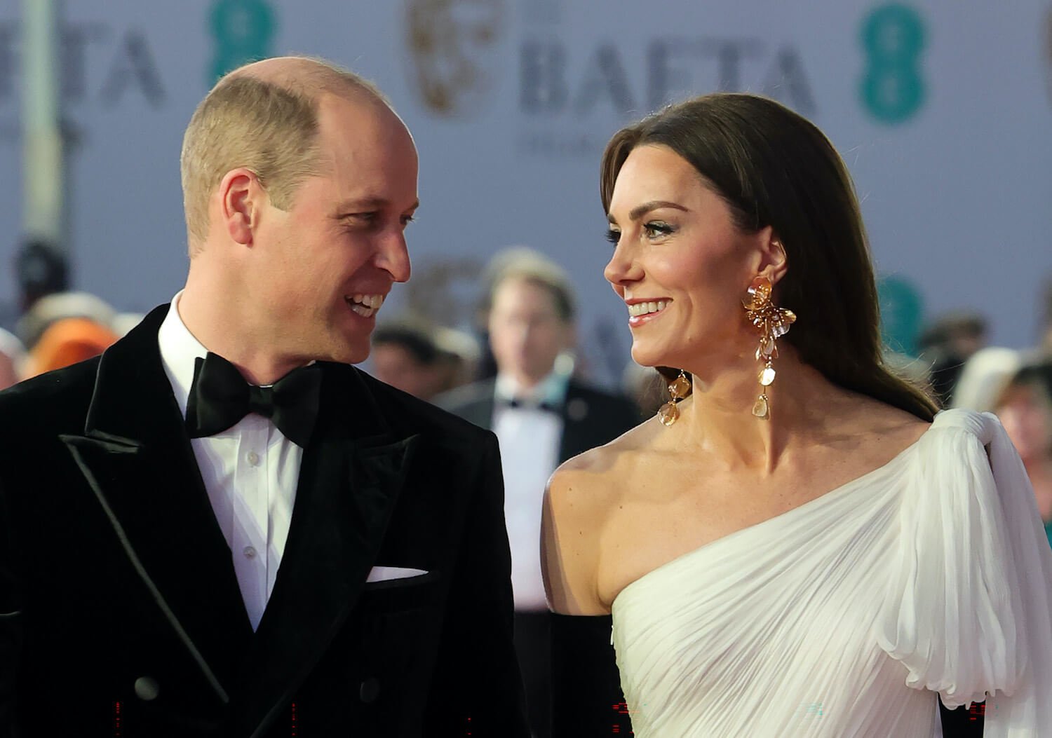 Kate Middleton wears a white gown as she smiles and looks at husband Prince William, dressed in a tuxedo.