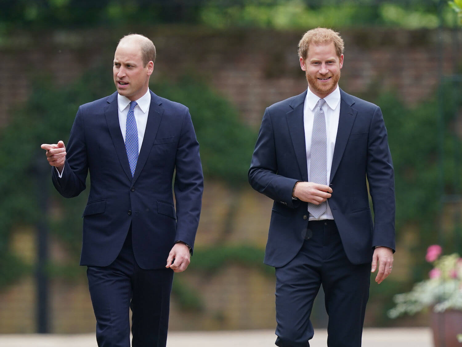 Prince William and Prince Harry walk side by side with Harry smiling, both dressed in dark suits