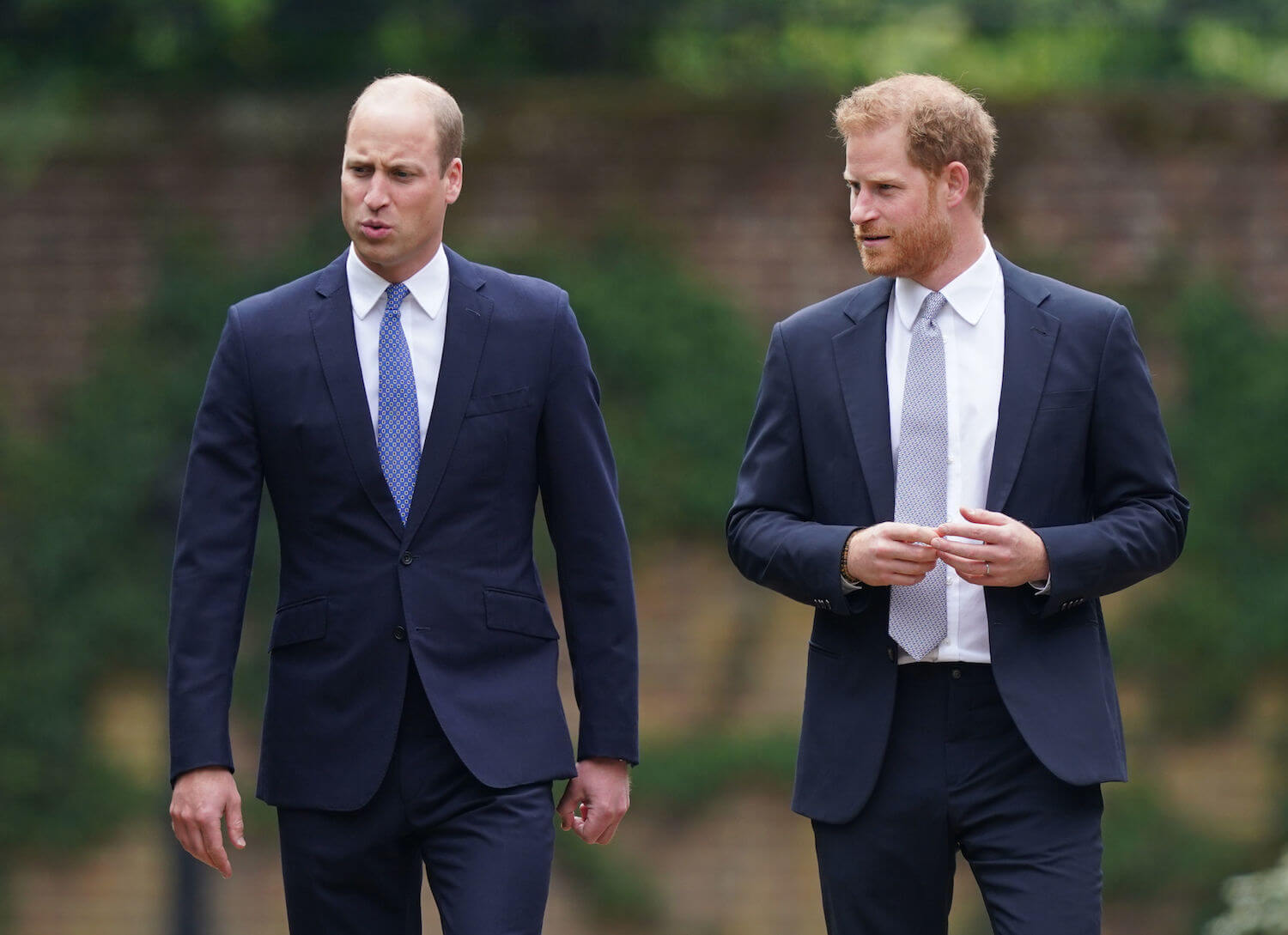 Prince William and Prince Harry walk and talk together, wearing dark suits