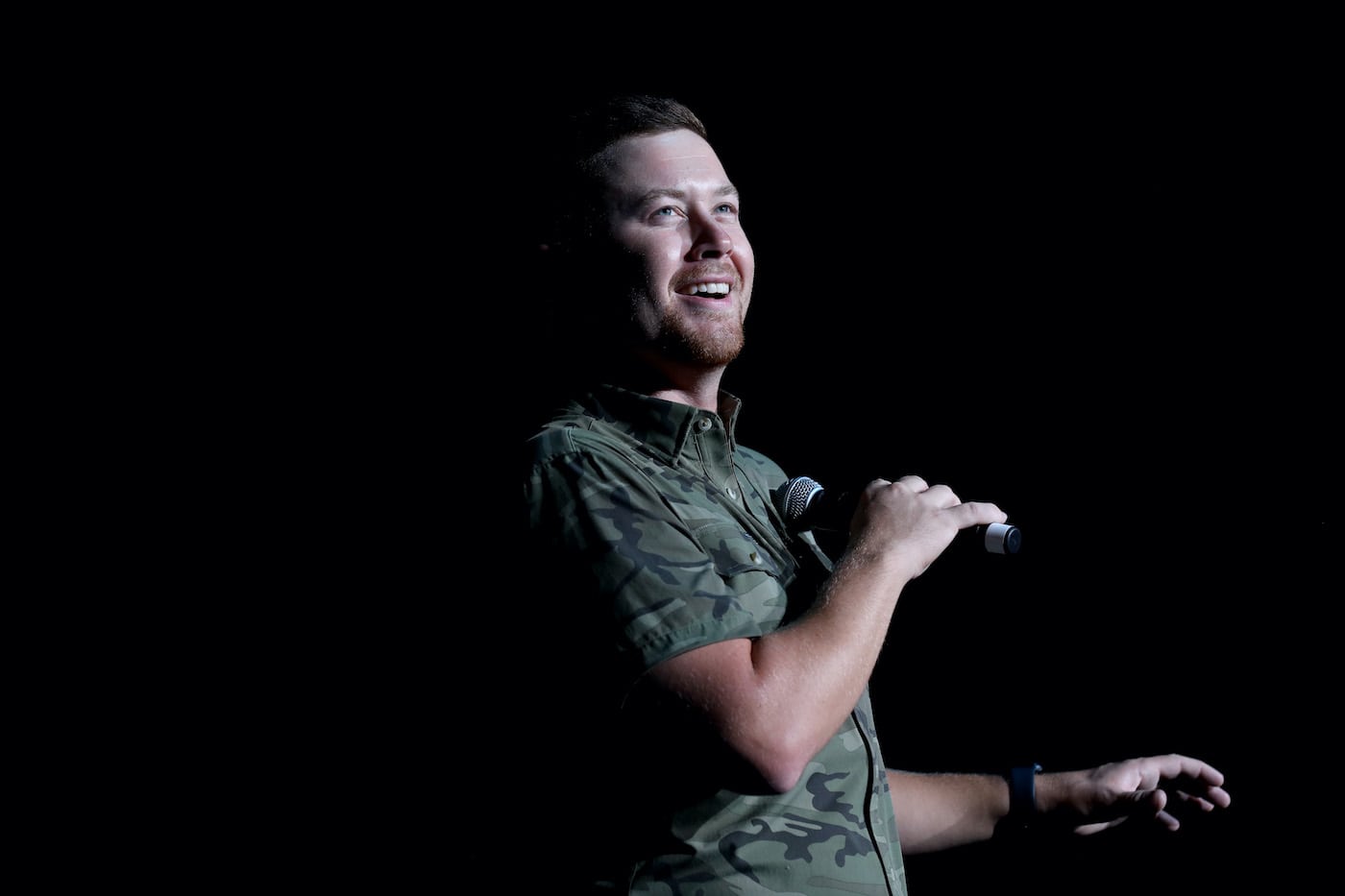 Scotty McCreery performs and holds a microphone and smiles