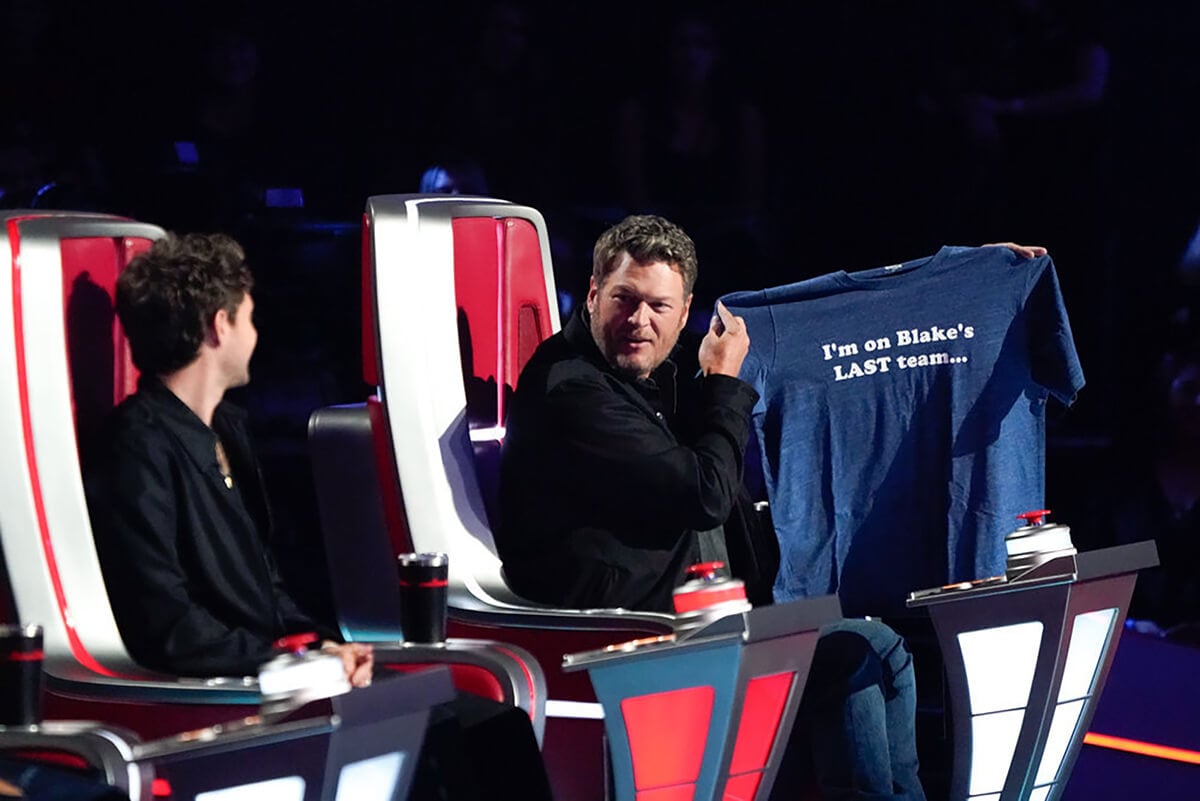 The Voice: Niall Horan looks at Blake Shelton holding up his coach gift, a blue T-shirt that reads, 'I'm on Blake's last team...'