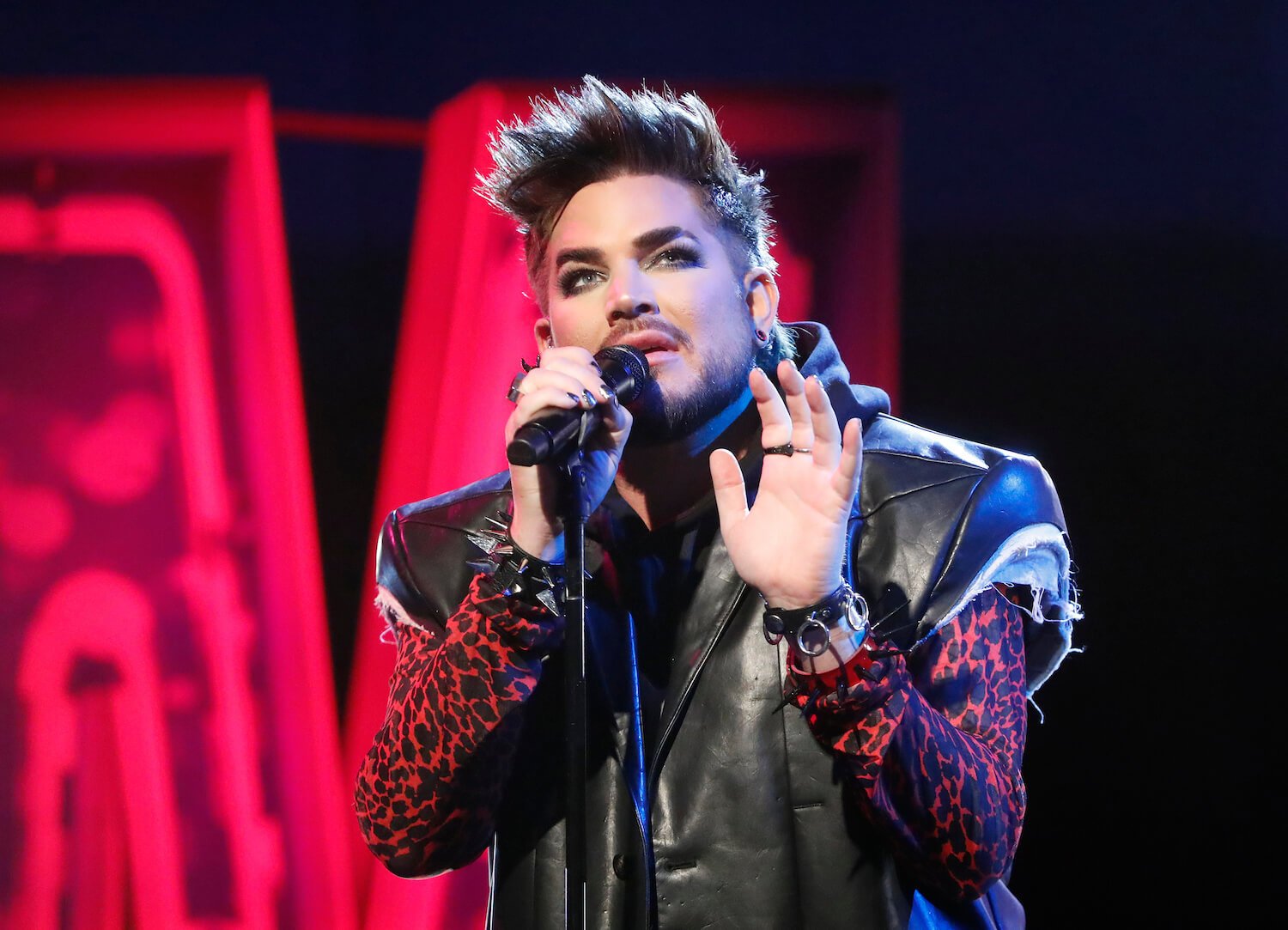 Adam Lambert from 'American Idol' singing into a microphone against a red and black background