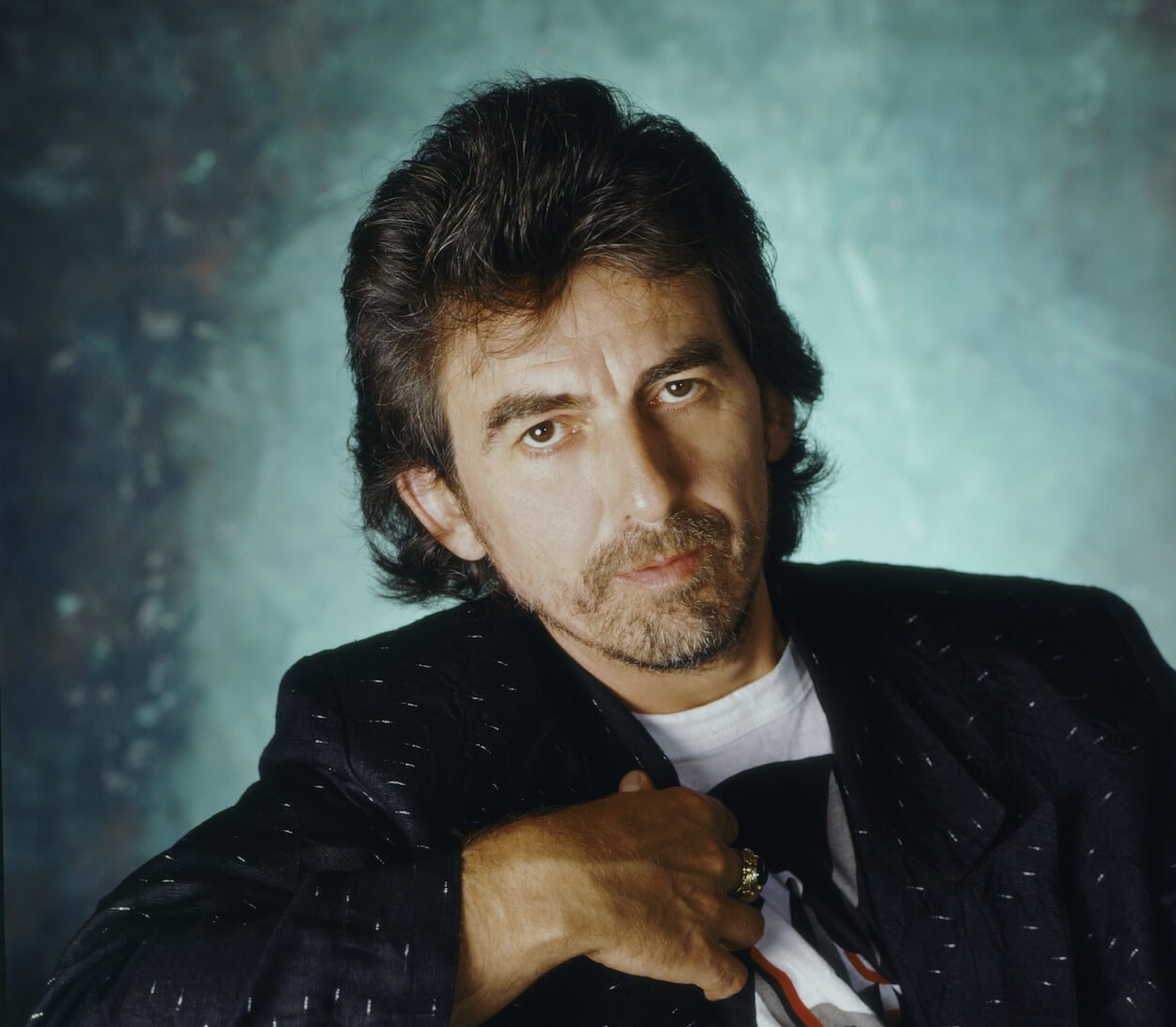George Harrison sports a light beard and wears a dark suit jacket while posing for a portrait.