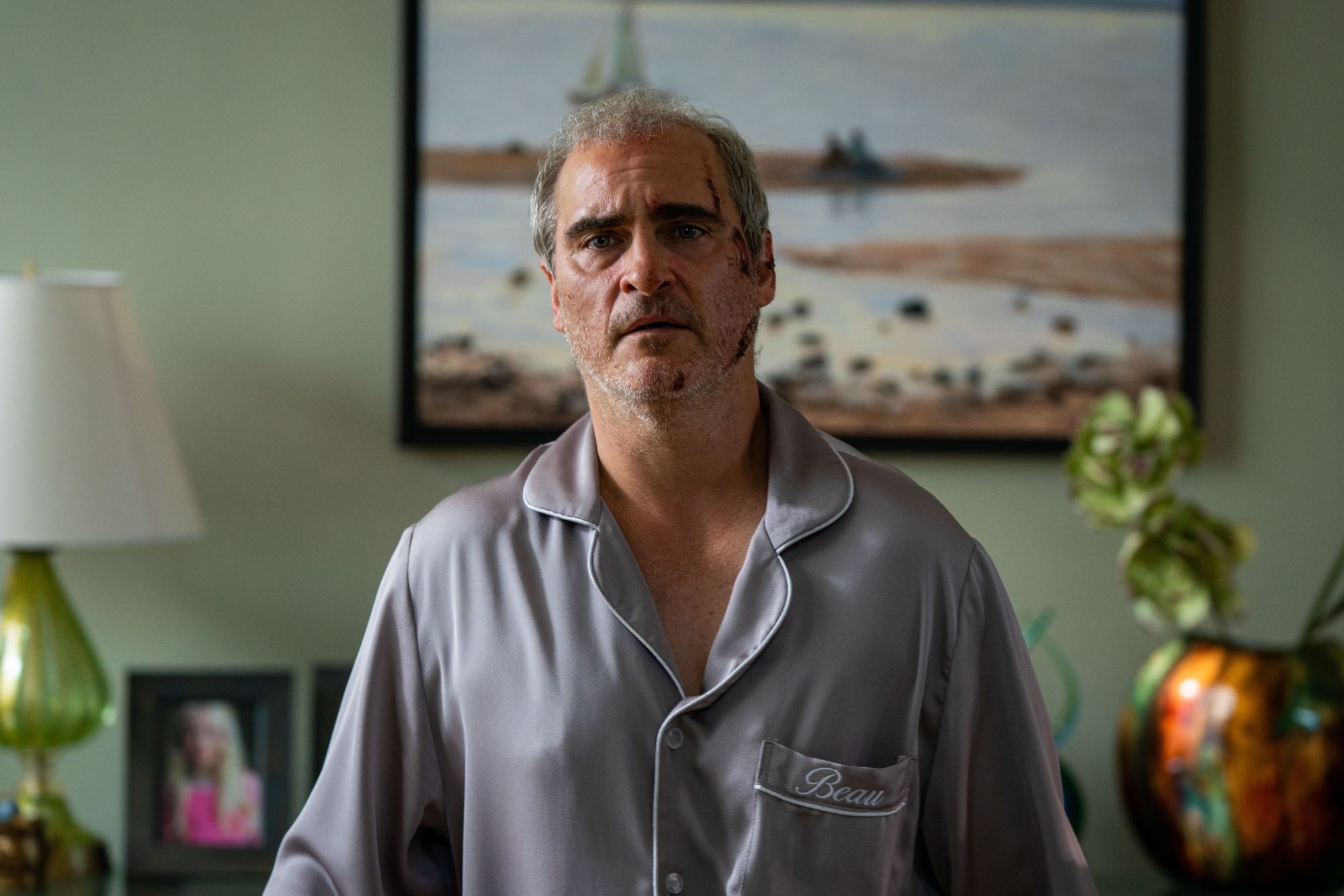 'Beau Is Afraid' Joaquin Phoenix as Beau looking worried, while wearing pajamas. A painting is on the wall behind him.