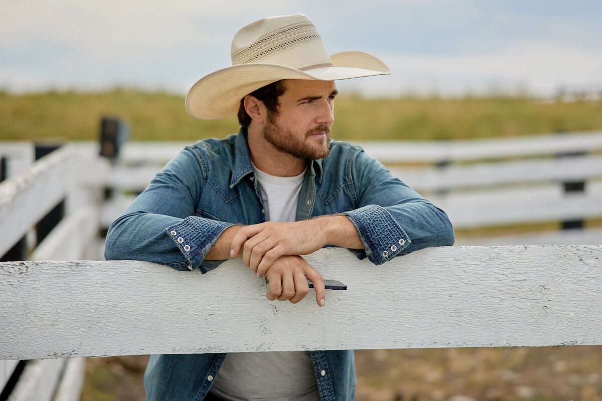 'Ride' actor Beau Mirchoff as Cash, wearing a cowboy hat and leaning on a fence, in the Hallmark Channel series