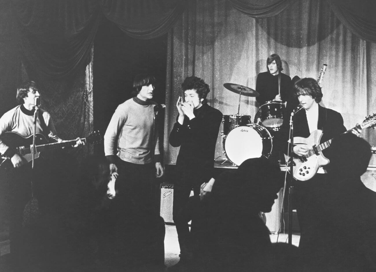 A black and white picture of Bob Dylan playing harmonica while performing with The Byrds. 