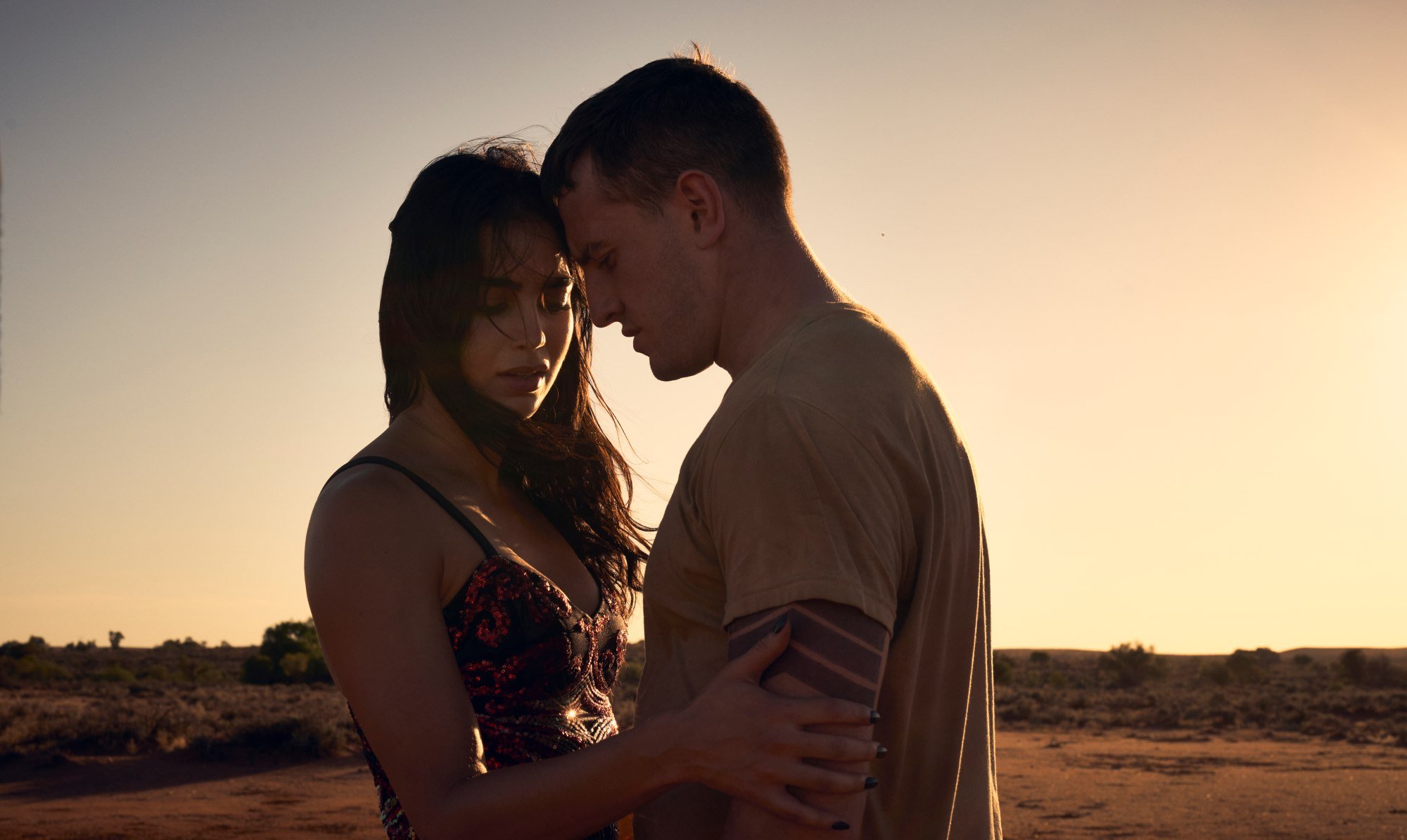 'Carmen' Melissa Barrera as Carmen and Paul Mescal as Aidan. They're standing in the desert, with her holding onto his arm and he's looking down.