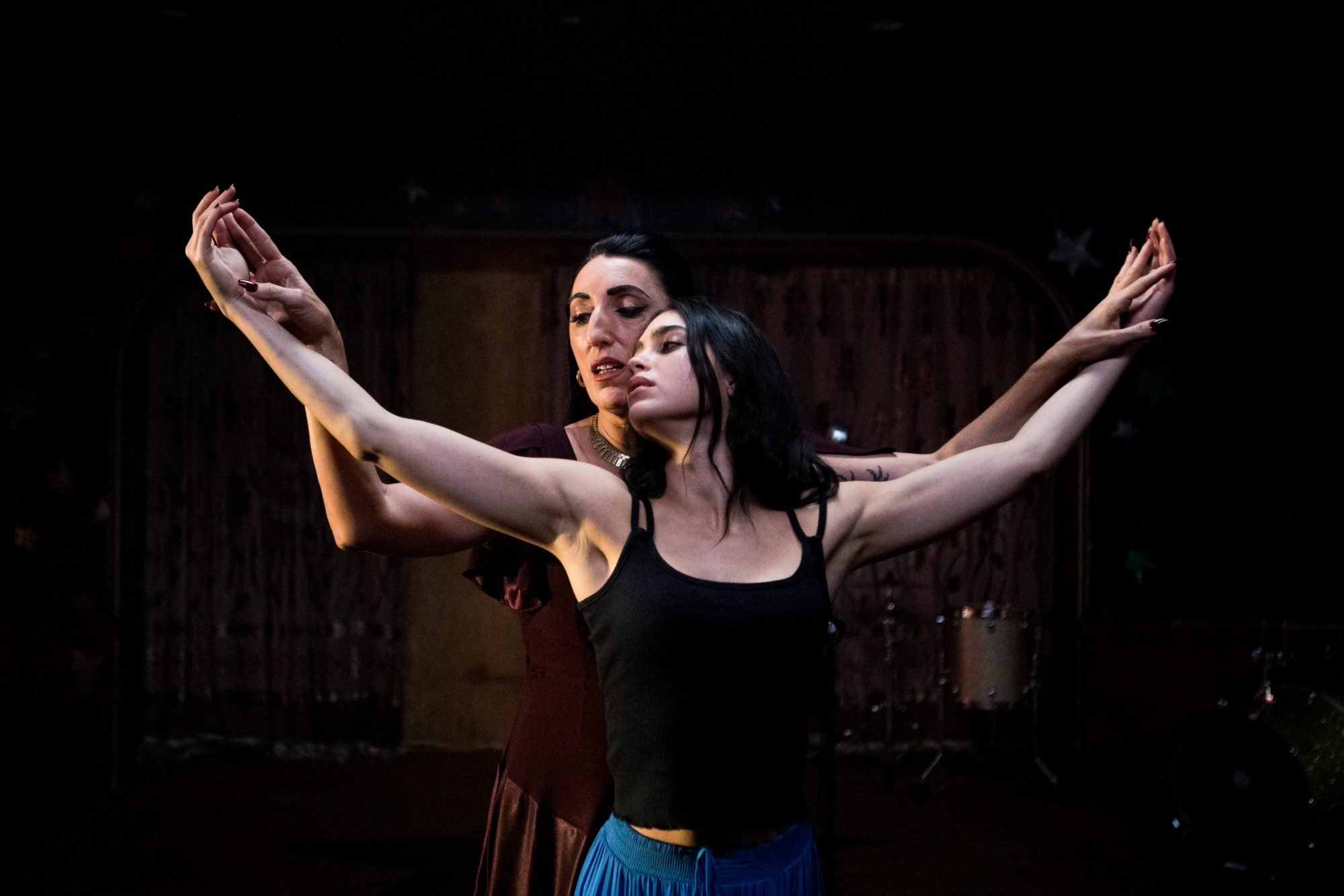 'Carmen' Rossy de Palma as Masilda and Melissa Barrera as Carmen. Masilda is standing behind Carmen, with both of their arms raised. 