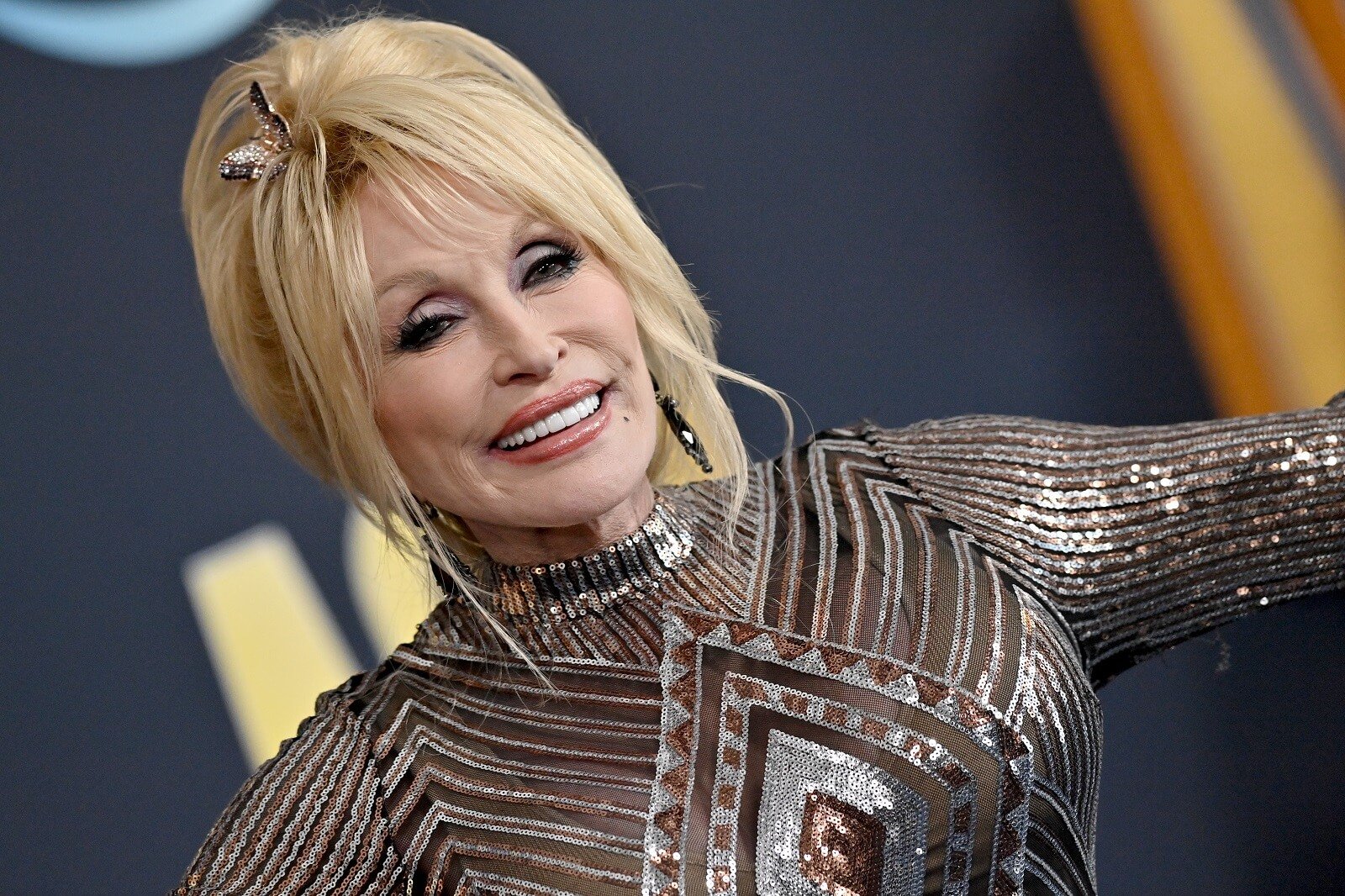 Dolly Parton smiles in a gold and silver shimmery dress