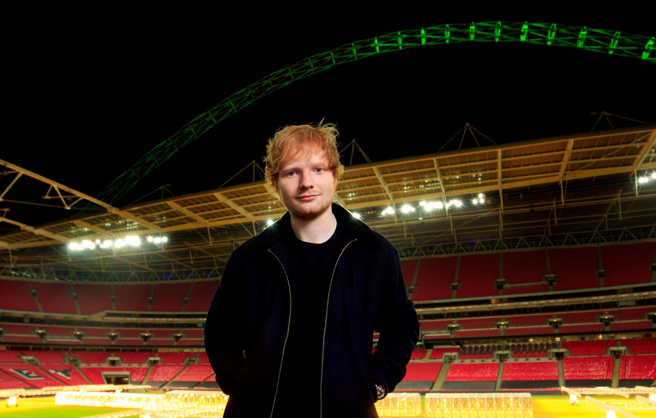 Ed Sheeran stands in front of an empty stadium.