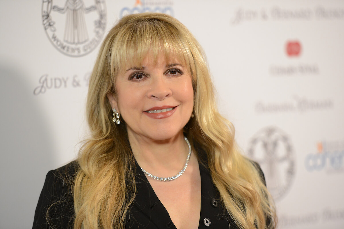 Fleetwood Mac singer Stevie Nicks smiles and poses at an event in her signature all-black outfit.