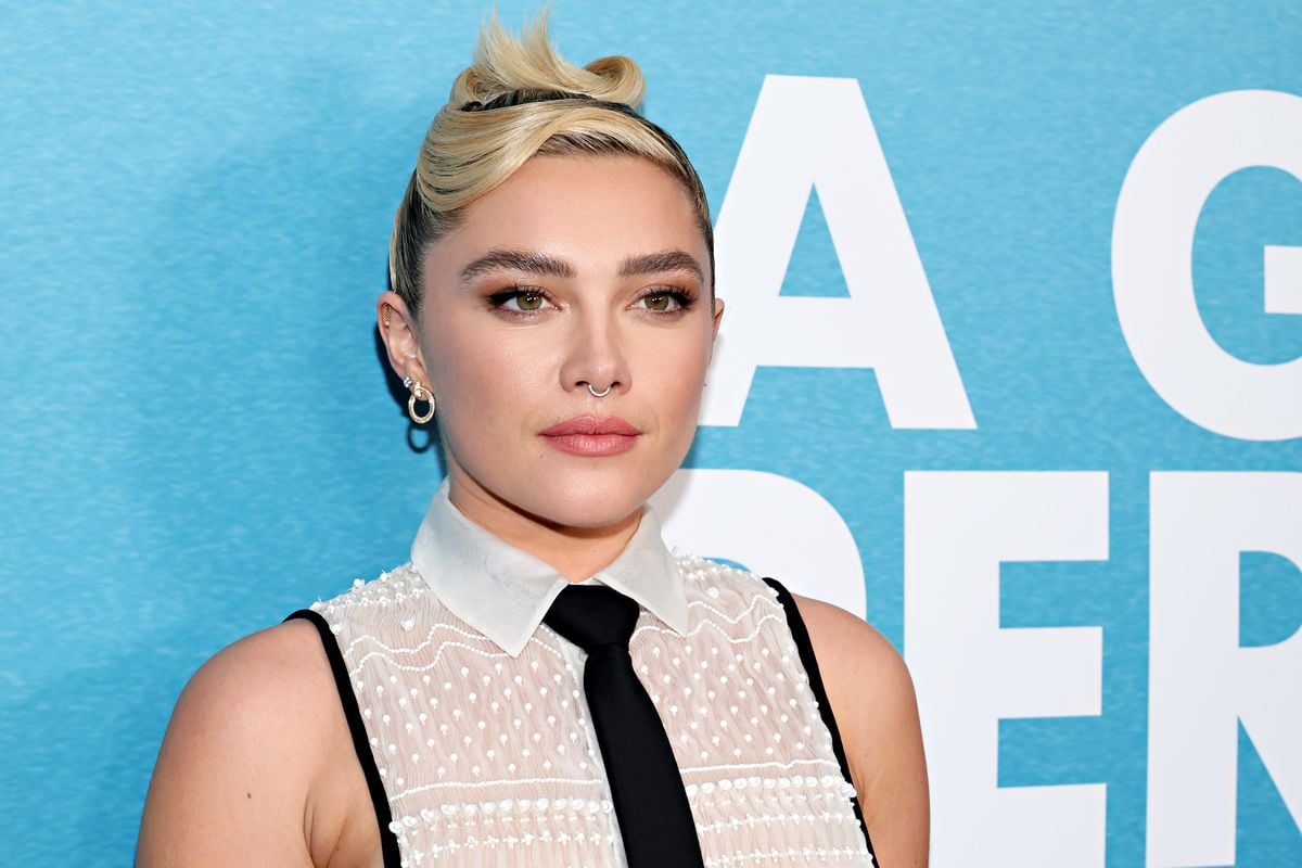 Florence Pugh poses for a photo in front of a blue backdrop.