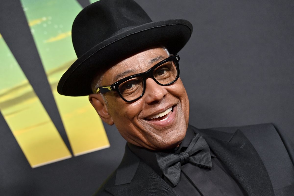 Giancarlo Esposito smiles for a photo in front of a backdrop featuring the logo for "The Mandalorian"