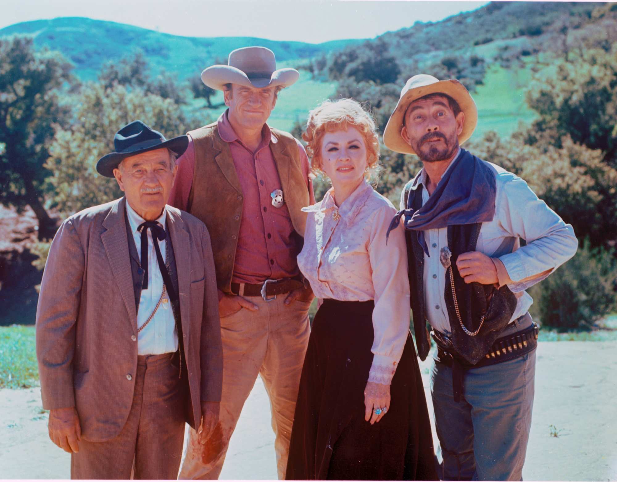 'Gunsmoke' cast wearing props, Milburn Stone as Doc Adams, James Arness as Matt Dillon, Amanda Blake as Miss Kitty, and Ken Curtis as Festus Haggen standing in a cast portrait in-costume.