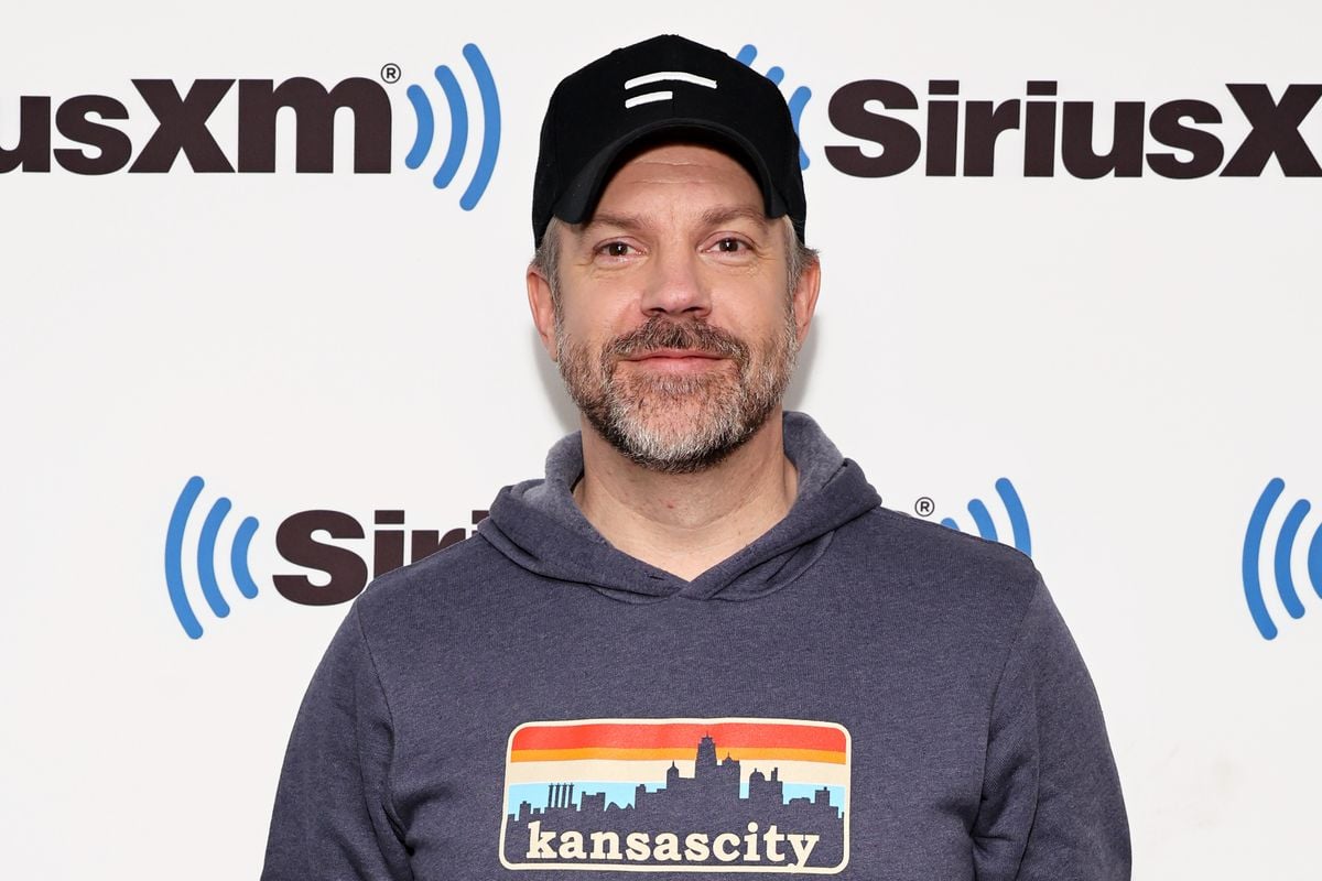 Jason Sudeikis poses in front of the Sirius XM logo.