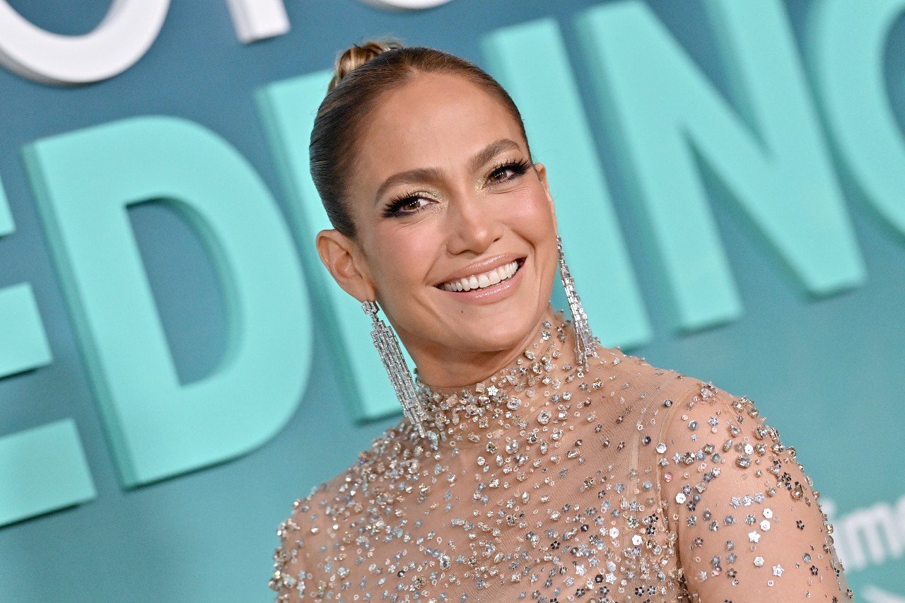 Jennifer Lopez smiles and wears a sparkly dress during a media event.