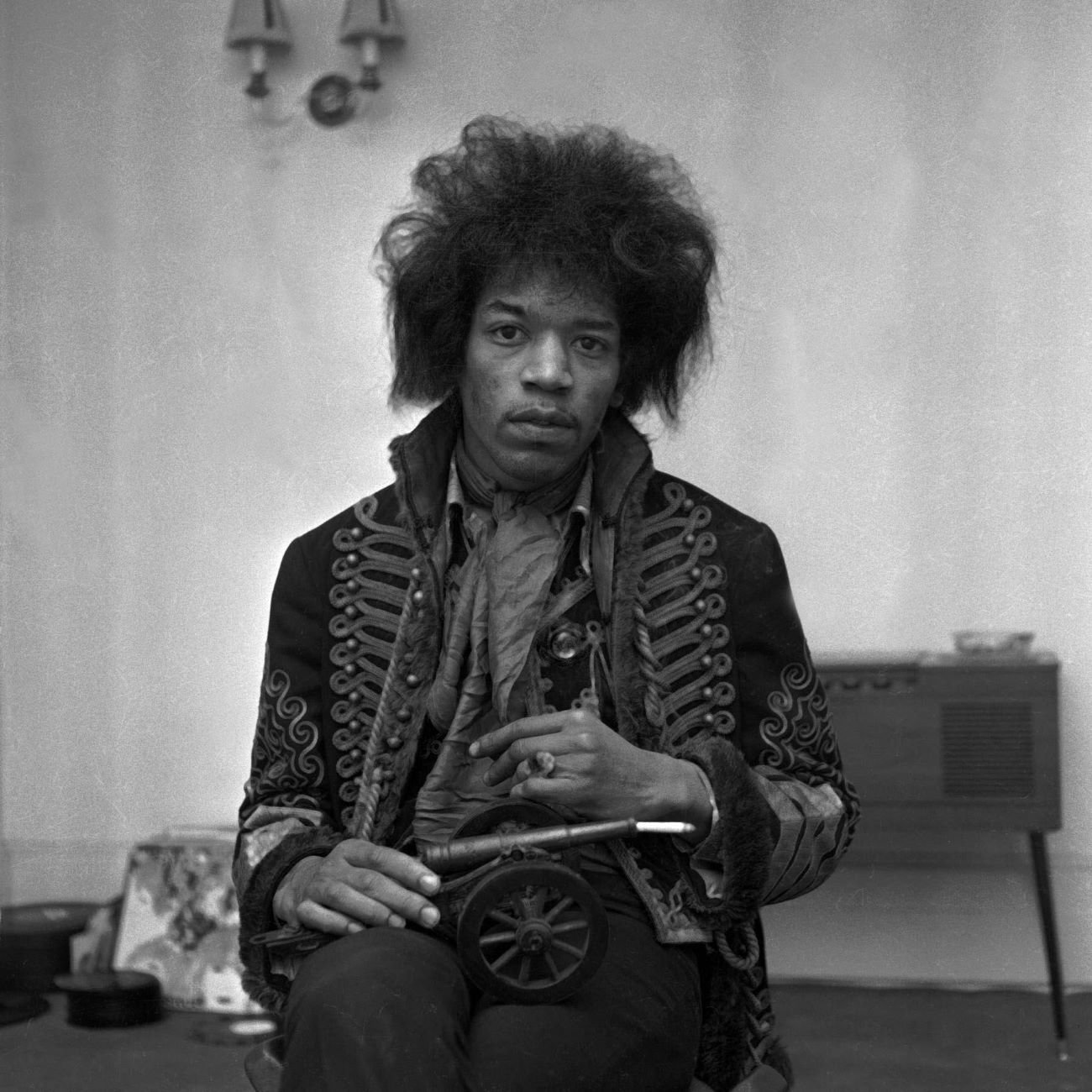 A black and white picture of Jimi Hendrix sitting with a miniature cannon in his lap.