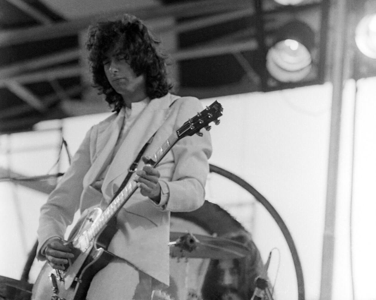 Led Zeppelin's Jimmy Page wears a light-colored suit while playing guitar during a 1973 concert.