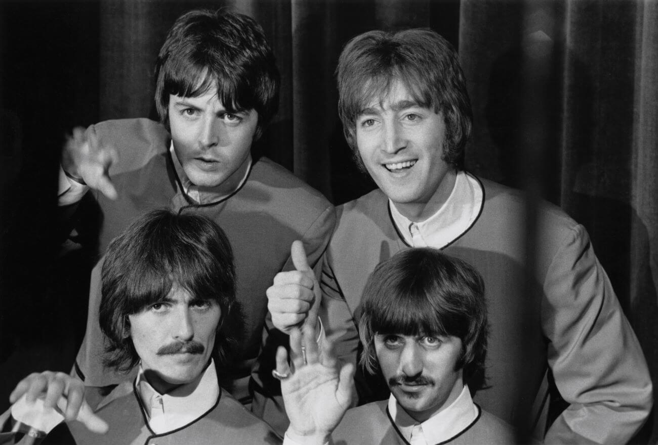 A black and white picture of Paul McCartney, John Lennon, George Harrison, and Ringo Starr wearing matching outfits and holding up their hands.