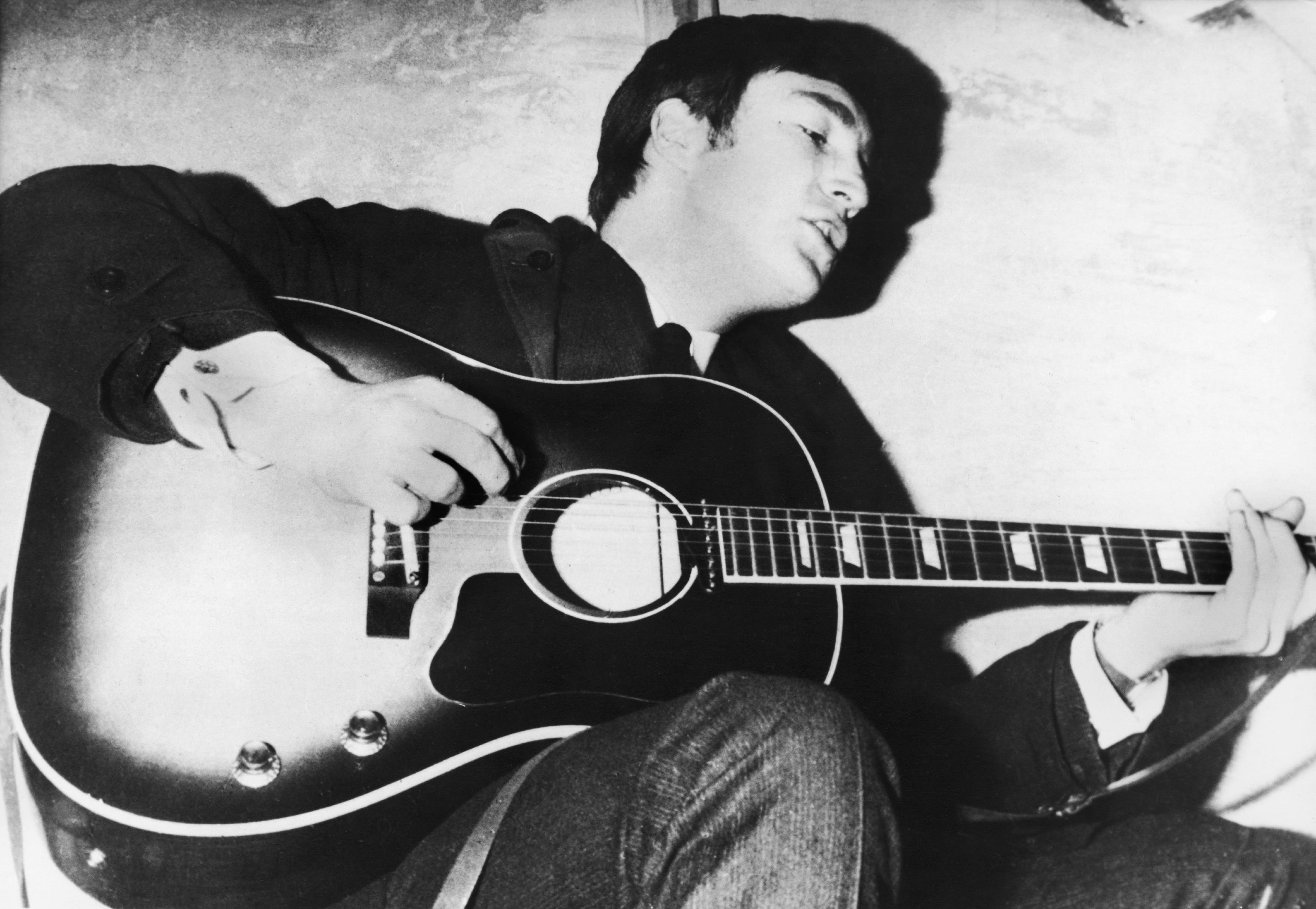 John Lennon playing his guitar in black and white, sometime around 1960.