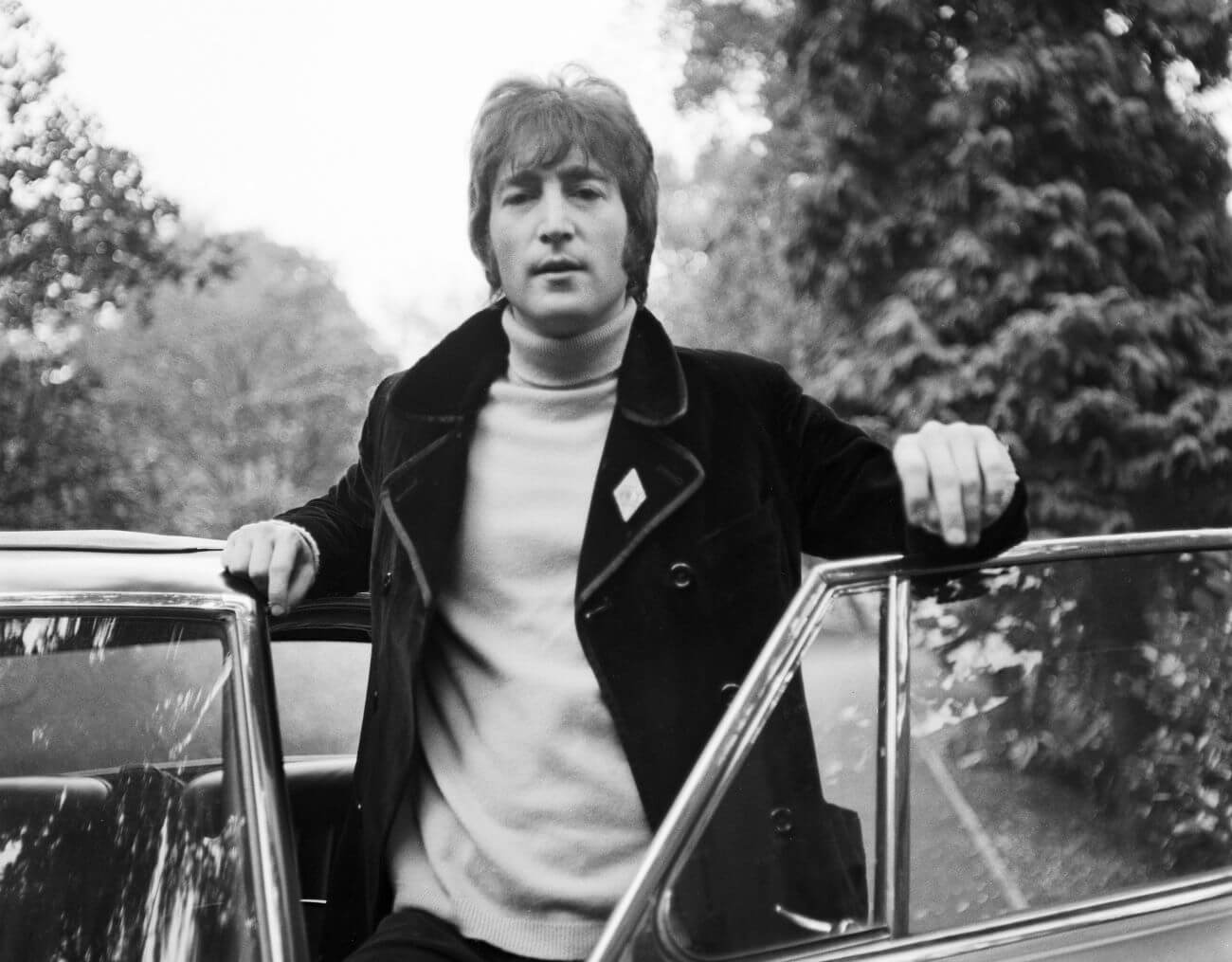 A black and white picture of John Lennon standing behind an open car door.