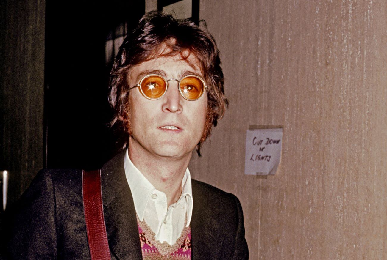 John Lennon wears a jacket and wears orange tinted glasses.