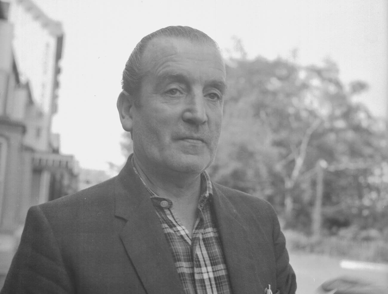 A black and white picture of John Lennon's father Fred wearing a plaid shirt and a blazer.