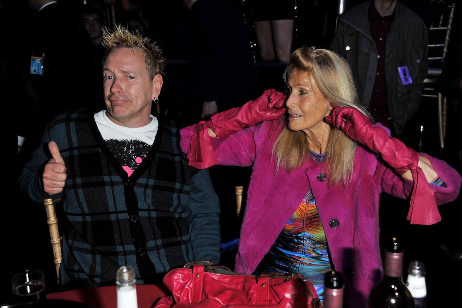 John Lydon, aka Johnny Rotten, and wife Nora Forster sitting next to each other. Johnny Rotten and Nora Forster have a 13-year age gap.