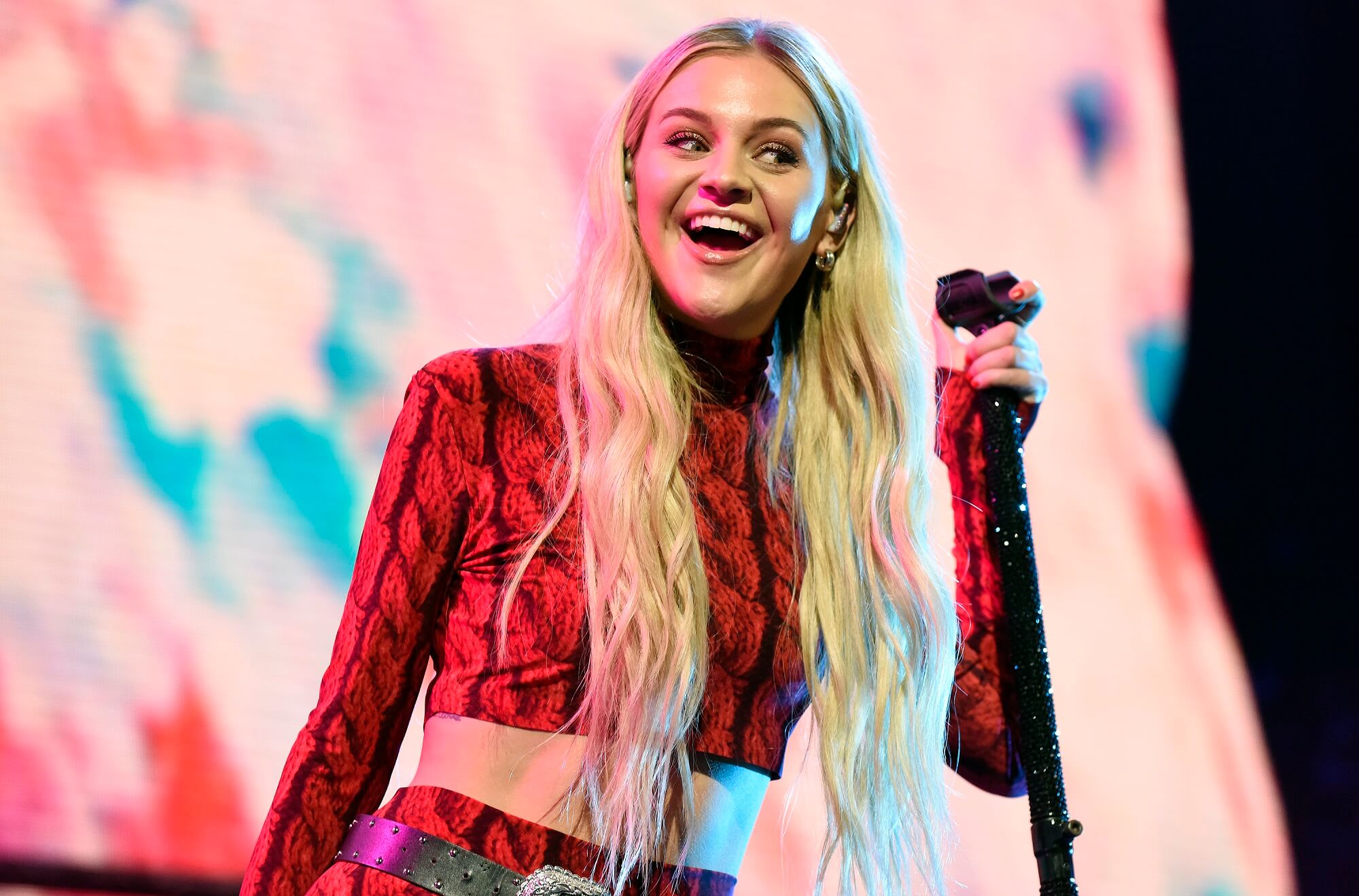 Kelsea Ballerini smiles on stage while holding a microphone stand