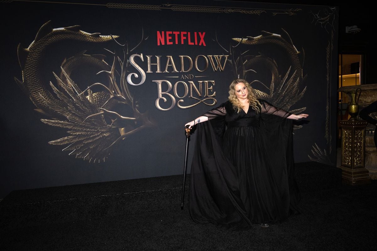 Leigh Bardugo poses in front of a backdrop featuring the "Shadow and Bone" logo. 